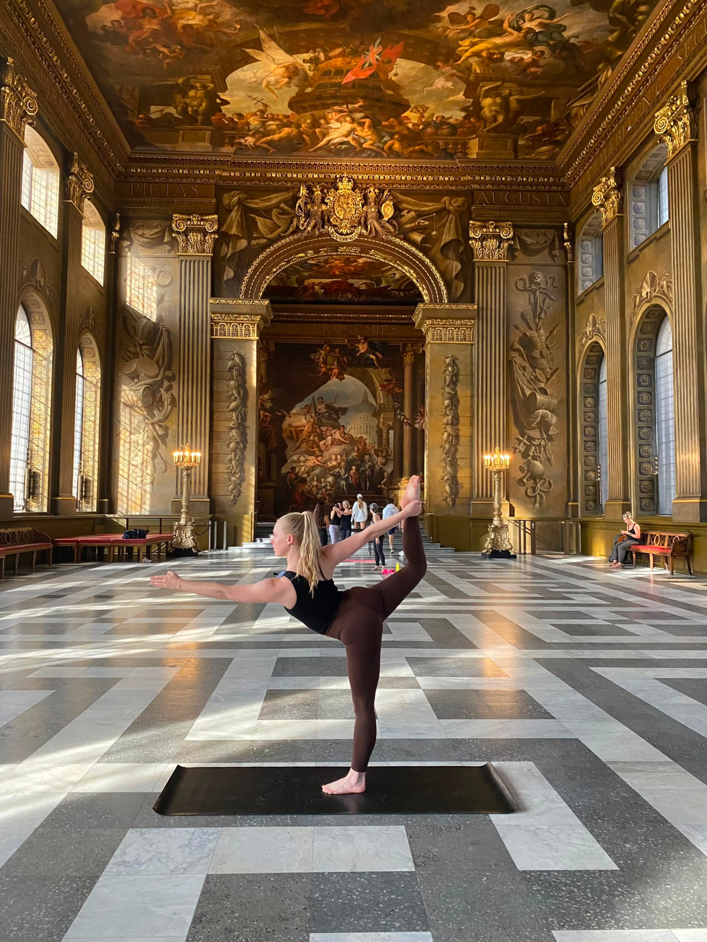 Abbie in a standing balance yoga pose inside a grand painted hall
